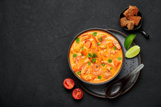 moqueca con pescado y camarones en tazón negro sobre mesa de pizarra oscura. plato de curry de marisco brasileño con leche de coco y verduras. vista superior. copiar espacio - moqueca fotos fotografías e imágenes de stock