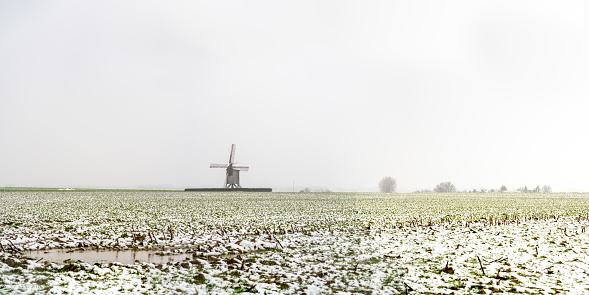 During snowing at the Vinke windmill (Vinkemole) with a gray sky and snow on the field