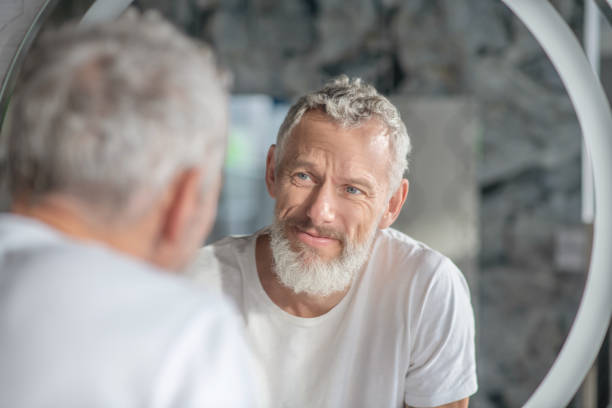 istock Grey-haired man looking at his reflection in the mirror 1297175525