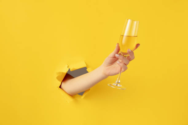 シャンパンフルートで美しい女性の手は黄色の背景を突破 - champagne toast wine restaurant ストックフォトと画像