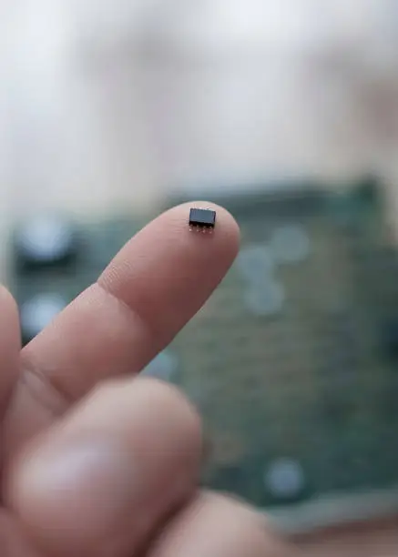 A tiny microchip on the finger of a man's hand against the background of a circuit board.The concept of technology and the evolution of computer science
