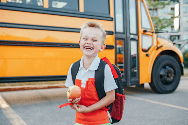 最初の9月の日に黄色いバスで笑う白人の少年の学生を幸せに笑う。屋外の校庭でリンゴの果物を食べる子供の話が聞こえにくい。教育と秋の秋に学校に戻ります。 - child eating apple fruit ストックフォトと画像