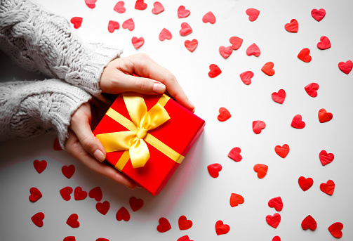 hands hold a gift on a white background with red hearts.
