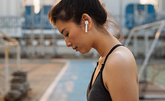 Close up: outdoor portrait of a fit Asian runner wearing wireless earphones