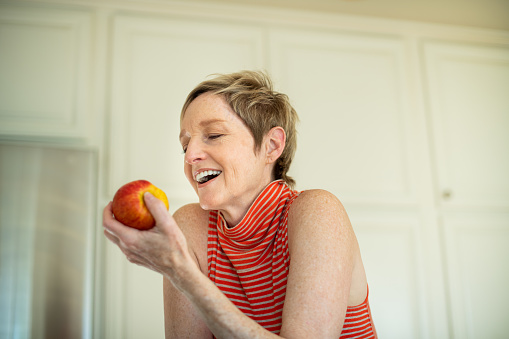 Stylish woman with a great smile and teeth leans on her kitchen counter while eating an apple.