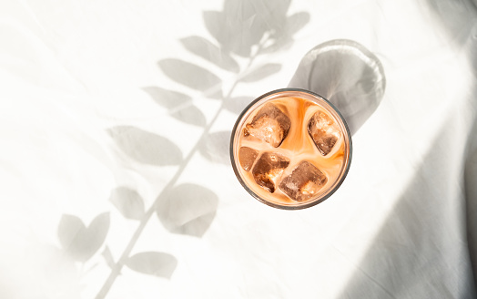 Cup of ice coffee with milk in white bed. Cold brew coffee. Flatlay, top view. Minimalism. Morning with sunlight.