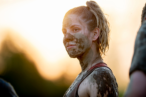 A young female adult of Caucasian ethnicity is participating at a mud run competition. Her face is covered with mud and she appears determined to win.