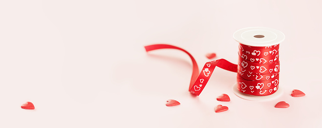 A roll of red gift ribbon with sprinkles hearts for St Valentines day or 14 February. Minimal banner with copy space