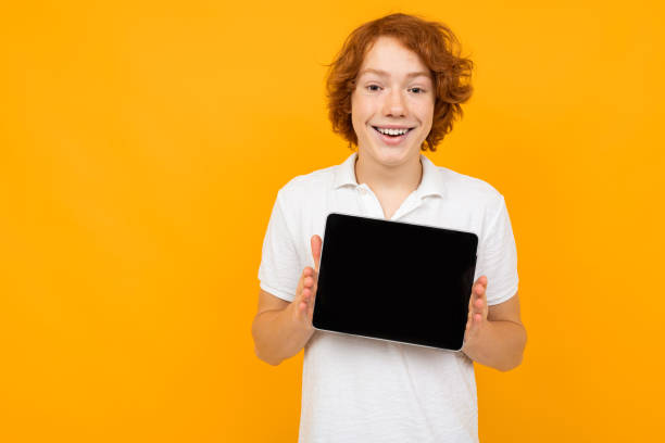 istock Caucasian guy in a white shirt shows a blank tablet screen template on a yellow background with copy space 1297197587