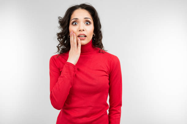 istock surprised brunette girl in a red sweater on a gray studio background with copy space 1297198452