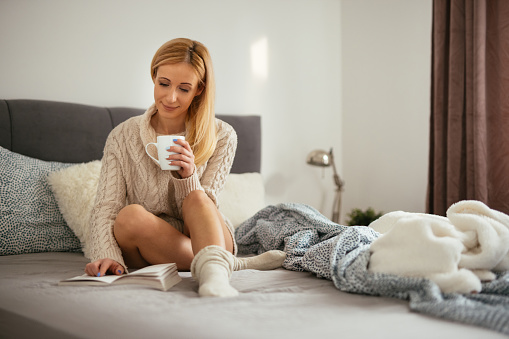Young woman enjoying a good book at home in bed while drinking coffee