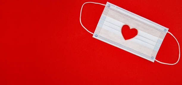 istock Medical mask with heart shape on red background 1297202259
