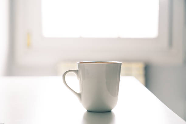 istock White coffee mug on a white desk with the light from a window 1297204341