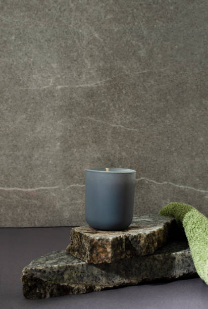 vertikale iamge. aroma-kerze auf dem stapel von marmorstücken, grünes handtuch gegen graue wand. konzept der badeentspannung - aromatherapy candles stock-fotos und bilder