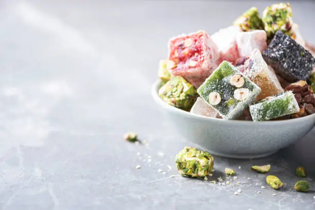 Middle Eastern sweets. Turkish delight with pistachios nuts on grey background. Copy space. Arab dessert, rahat lokum, sherbet, nougat, churchkhela, cookies. Macro shoot