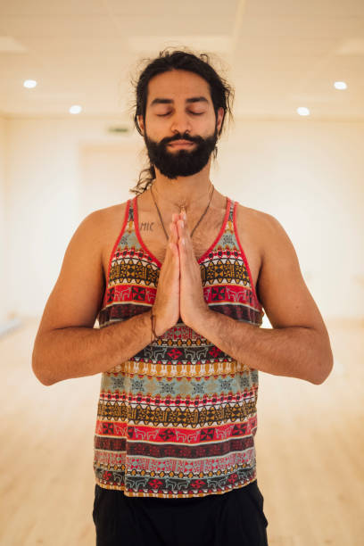 Finding Inner Peace Waist up view of a man doing yoga during lockdown in the Covid 19 pandemic. He is standing with his hands together in prayer pose and his eyes are closed. man yoga tattoo stock pictures, royalty-free photos & images
