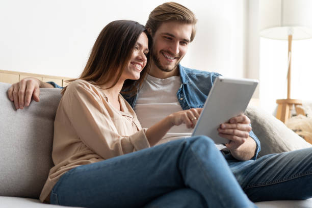 istock Young couple sitting on couch at home, using a tablet PC for Internet and social media. 1297217301
