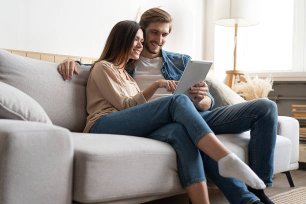 istock Young couple sitting on couch at home, using a tablet PC for Internet and social media. 1297217302