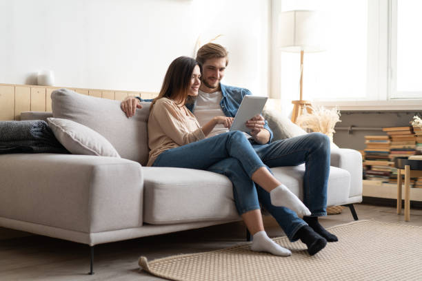 istock Young couple sitting on couch at home, using a tablet PC for Internet and social media. 1297217303