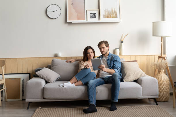 istock Young couple sitting on couch at home, using a tablet PC for Internet and social media. 1297217310