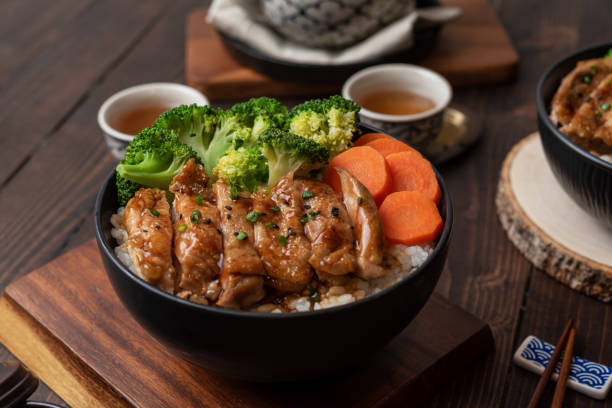 일본 식스타일 : 밥, 당근, 브로콜리를 곁들인 홈메이드 치킨 데리야키의 최고 전경을 검은 그릇에 얹고 나무 테이블에 놓습니다. - teriyaki broccoli carrot chicken 뉴스 사진 이미지