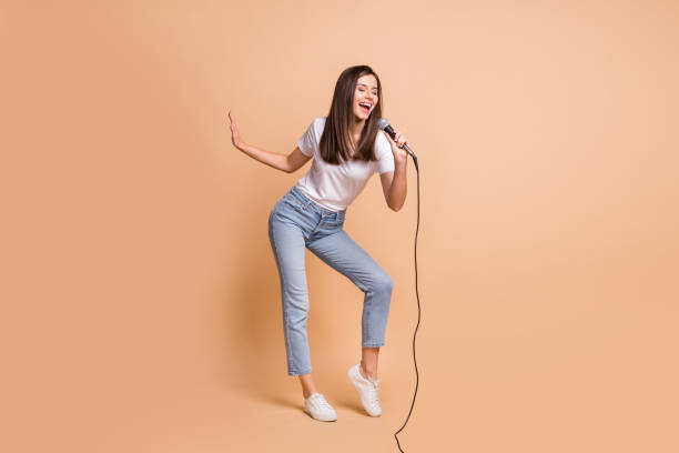 foto de tamaño corporal de longitud completa de la canción de la estrella del pop femenina manteniendo el micrófono bailando en el escenario aislado en el fondo de color beige pastel - cantar fotografías e imágenes de stock