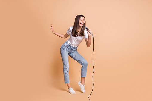 Full length body size photo of female pop star singing song keeping mic dancing on stage isolated on pastel beige color background.