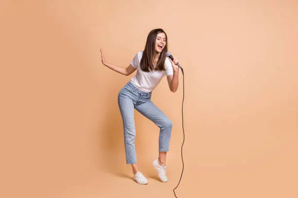 Photo of Full length body size photo of female pop star singing song keeping mic dancing on stage isolated on pastel beige color background