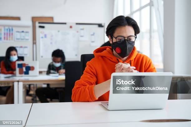 Smart Guy Is Sitting At The Table Opposite A Laptop And Looking At The Screen Stock Photo - Download Image Now