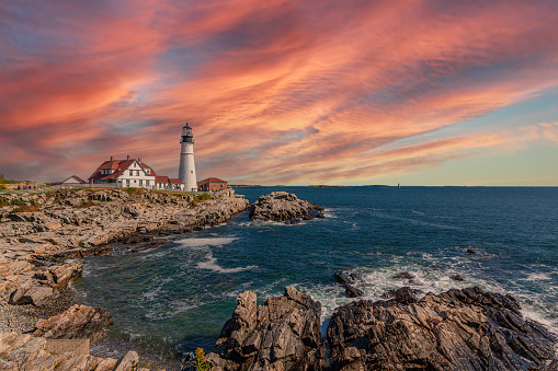 Portland Head Lighthouse, Cape Elizabeth, Maine, lit by the Morning Sun. Rocky Coastline with Cliffs, Ocean Surf and Blue Sky are in the image. Wide angle lens.
