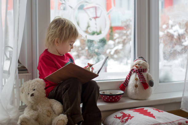 nettes blondes kleinkind kind, sitzend am fenster, blick auf den schnee fallen draußen - lesen regen stock-fotos und bilder
