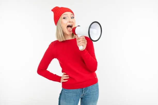 Photo of girl in red clothes with a megaphone in hands shouts on a white background