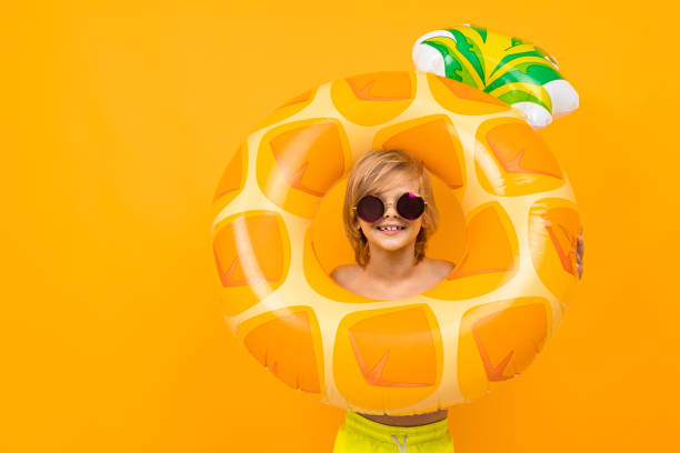 istock Handsome boy in swimming trunks holds a rubber ring, smiles and gesticulates isolated on orange background 1297226267