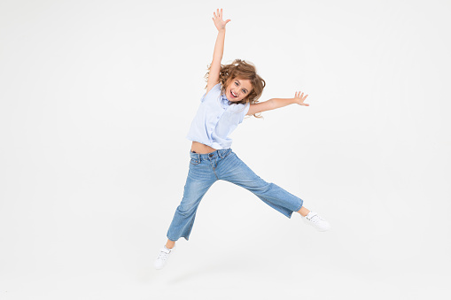 young girl in jeans jumping with happiness on a white background with copy space.