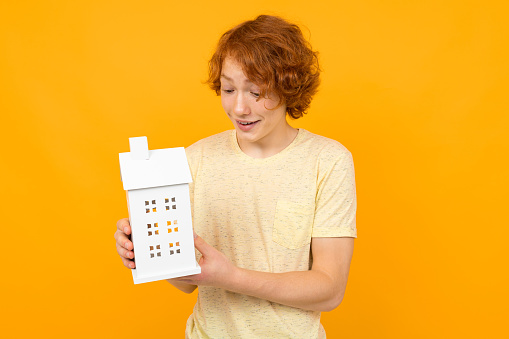 Real Estate Agent guy holds a house model in his hand on a yellow background with copy space.