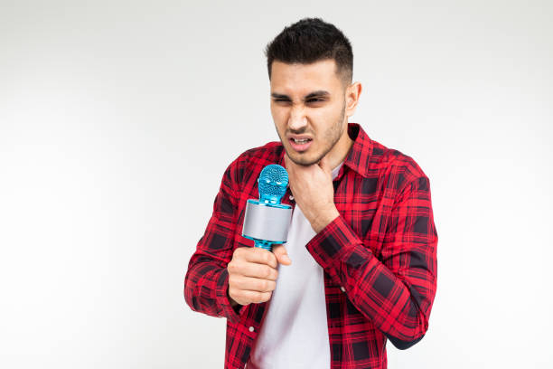 presentatore maschio con un microfono tra le mani ha mal di gola su uno sfondo bianco isolato studio - male singer singing men foto e immagini stock