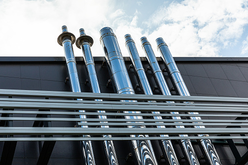 A lot of metal pipes stick out of a large building outside