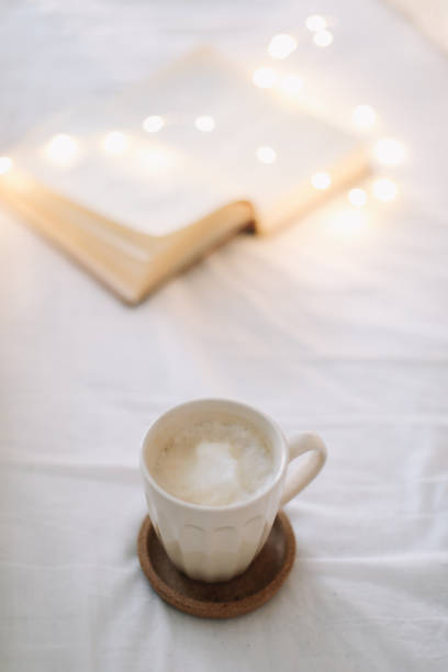 istock Coffee cup with milk foam and a book on a white bedsheet. 1297230476