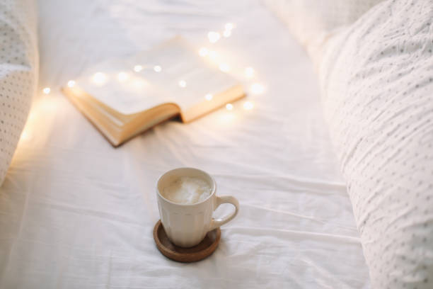 istock Coffee cup with milk foam and a book on a white bedsheet. 1297230629