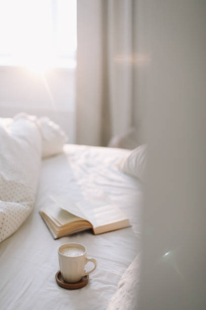 istock Coffee cup with milk foam and a book on a white bedsheet. 1297230680