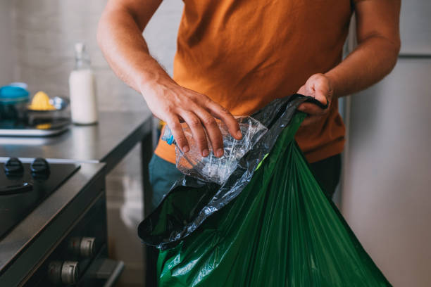 joven hombre caucásico anónimo poner una botella de plástico en una bolsa de basura de plástico - equipment housework remote domestic kitchen fotografías e imágenes de stock