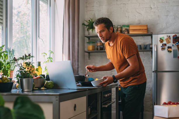 istock Handsome Young Man Making a Meal while Watching a Live Cooking Session in a Kitchen 1297236867