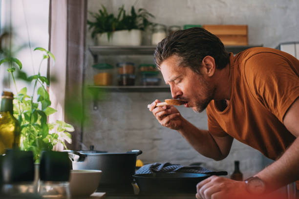 istock Handsome Young Man Tasting Sauce with a Mixing Spoon in a Kitchen 1297236877