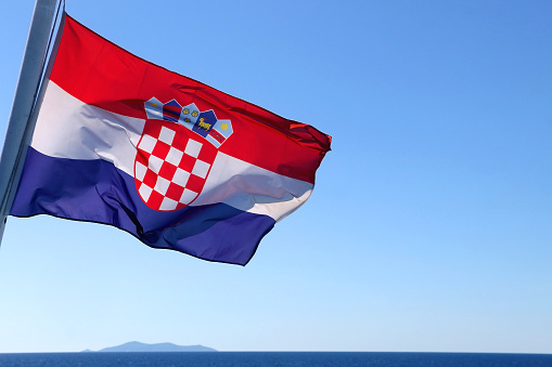 Flag of Croatia, blowing in the wind. Adriatic sea and bright sky in the background. Selective focus.