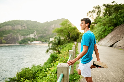 Young man standing by the road railing and stretching his leg after a run