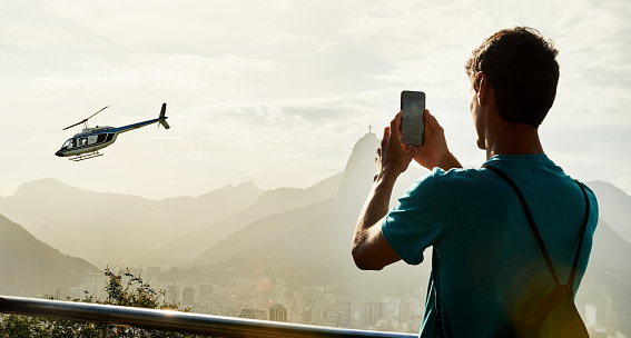 Rear view of a male tourist taking pictures of Rio De Janeiro city with a helicopter fly