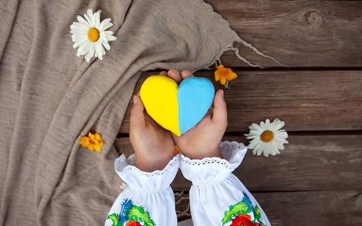 Un corazón amarillo y azul en las manos de un niño con una camisa bordada, sobre el fondo de una mesa de madera áspera y margaritas. Día de la Unidad, Día de la Independencia de Ucrania, Día del Bordado photo