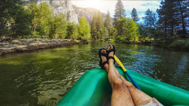 sommerurlaub in kalifornien: pov mann kreuz bein überquert entspannend beim rafting in merced river of yosemite - wildwasserkanufahren stock-fotos und bilder