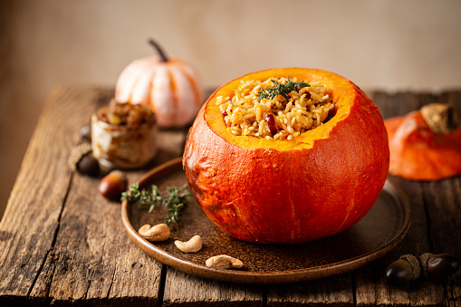 Tasty baked pumpkin stuffed with rice, vegetables, cashews and dried fruits on wooden table with dark background
