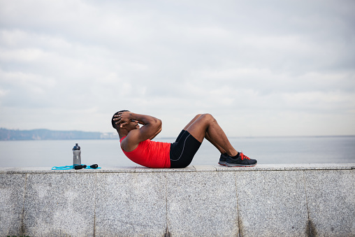 Man doing sit ups. Core outdoor workout. Black athlete exercising.